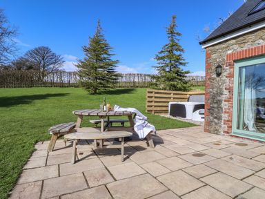 An outdoor patio with a wooden picnic table and bench on a paved area next to a stone building at Gwennol Cottage in Golden Grove near Llandeilo