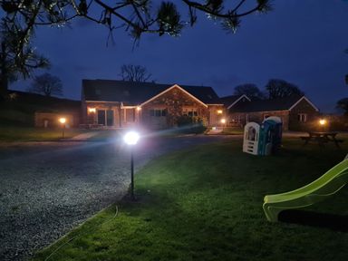 A house with outdoor lights along a driveway and a green slide and playhouse on a lawn at Gwennol Cottage in Golden Grove near Llandeilo