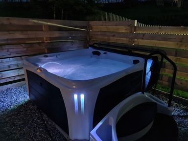 An outdoor hot tub with water jets illuminated at night surrounded by a wooden fence at Gwennol Cottage in Golden Grove near Llandeilo