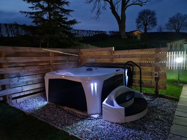 An outdoor hot tub with steps and wooden fencing around it at Gwennol Cottage in Golden Grove near Llandeilo