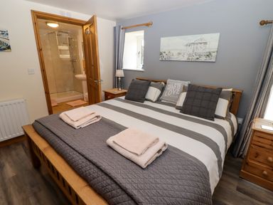 A bedroom with a bed striped bedding pillows bedside tables and an open door to a bathroom at Gwennol Cottage in Golden Grove near Llandeilo