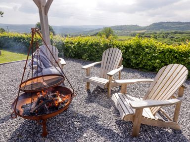 An outdoor seating area with three wooden chairs and a fire pit with a grill over it at Gwennol Cottage Golden Grove near Llandeilo