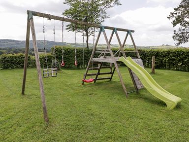 A wooden playground set with swings, a climbing ladder and a yellow slide on a grassy lawn