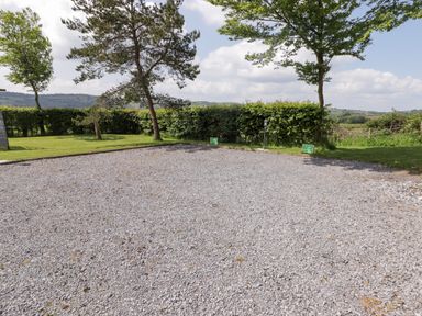 A gravel parking area bordered by grass and trees with farmland in the background at Gwennol Cottage in Golden Grove near Llandeilo