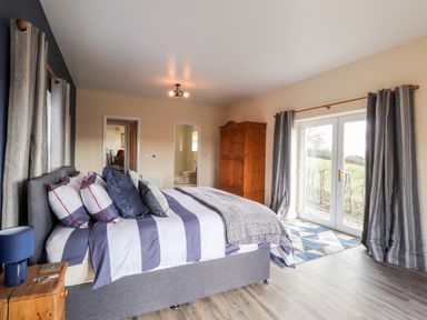 A bedroom with a bed a wooden wardrobe curtains and glass doors overlooking a garden at Sewin Cottage in Golden Grove near Llandeilo
