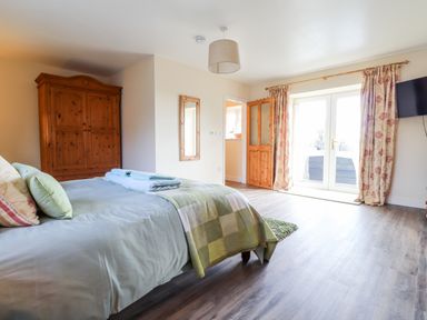 A bedroom with a bed towels wardrobe and doors leading outside at Sewin Cottage in Golden Grove near Llandeilo