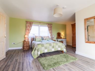 A bedroom with a double bed and green checkered blanket green rug wooden furniture and a window with floral curtains at Sewin Cottage in Golden Grove near Llandeilo