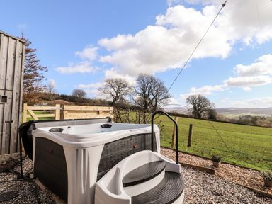 An outdoor hot tub with steps and a handrail on a gravel area overlooking fields and trees at Sewin Cottage in Golden Grove near Llandeilo
