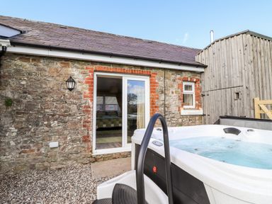 An outdoor hot tub next to a stone house with a sliding glass door and a wooden shed at Sewin Cottage Golden Grove near Llandeilo