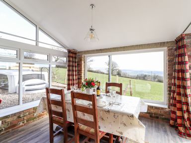 A dining area with a table set for four and large windows showing a grassy landscape at Sewin Cottage Golden Grove near Llandeilo