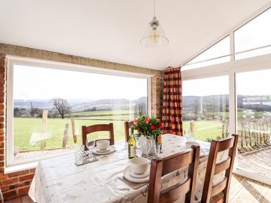 A dining area with a table set for four and large windows overlooking green fields at Sewin Cottage Golden Grove near Llandeilo