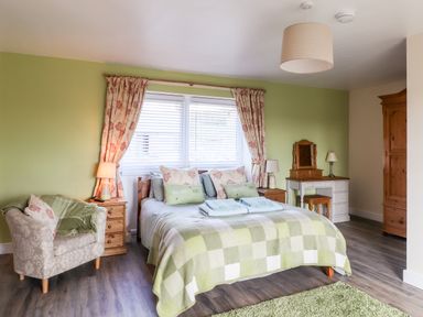A bedroom with a bed green checkered blanket bedside tables lamps armchair dressing table and wooden wardrobe at Sewin Cottage in Golden Grove near Llandeilo