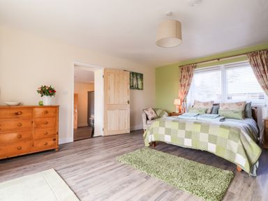 A bedroom with a bed covered by a green checkered blanket a wooden dresser with flowers and a chair near the bed at Sewin Cottage Golden Grove near Llandeilo