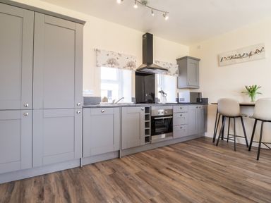 A kitchen with grey cabinets a built in oven a microwave and a small dining table with two chairs at Sewin Cottage Golden Grove near Llandeilo