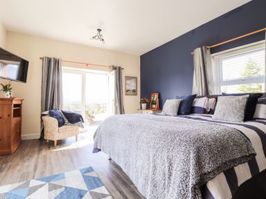 A bedroom with a large bed pillows an armchair a wooden cabinet curtains and a wall-mounted television at Sewin Cottage in Golden Grove near Llandeilo