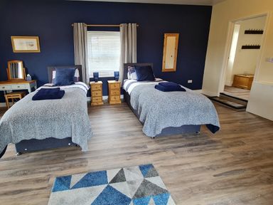 A bedroom with two single beds a window two wooden nightstands a dresser with a stool and a geometric patterned rug at Sewin Cottage Golden Grove near Llandeilo
