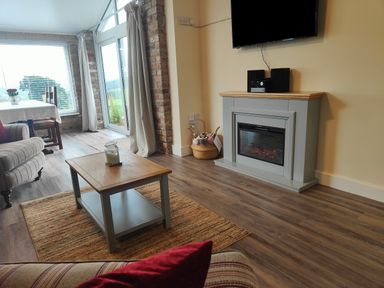 A living room with a coffee table a fireplace a wall-mounted television and glass doors at Sewin Cottage Golden Grove near Llandeilo