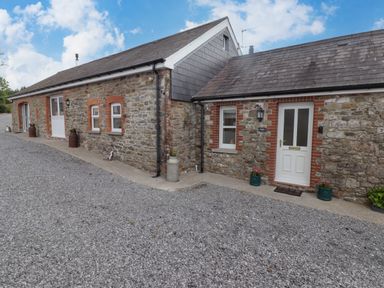 Exterior view of a stone cottage with white doors and small windows on a gravel driveway at Sewin Cottage in Golden Grove near Llandeilo