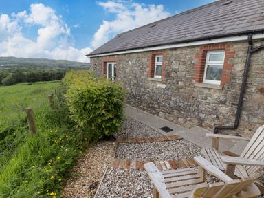 A stone cottage exterior with wooden chairs gravel pathway and green fields at Sewin Cottage in Golden Grove near Llandeilo