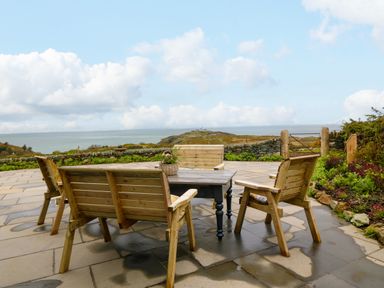 A patio with wooden chairs around a table and ocean view at Balog Farm in Amlwch