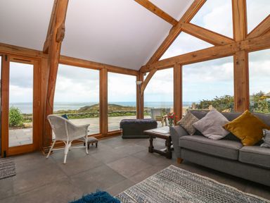 A living room with large wooden framed windows and a gray sofa with pillows at Balog Farm in Amlwch