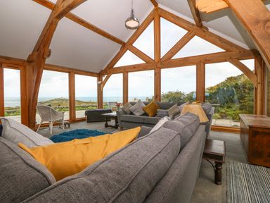 A living room with large windows wooden beams gray sofas and pillows at Balog Farm in Amlwch