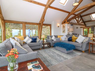 A living room with gray sofas and colorful cushions next to large windows with wooden beams at Balog Farm in Amlwch