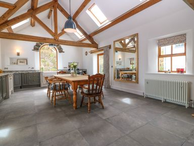 A kitchen dining area with wooden table and chairs stone tiled floor and exposed wooden beams at Balog Farm in Amlwch