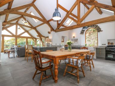 A dining and living area with wooden beams wooden table chairs and large windows at Balog Farm in Amlwch