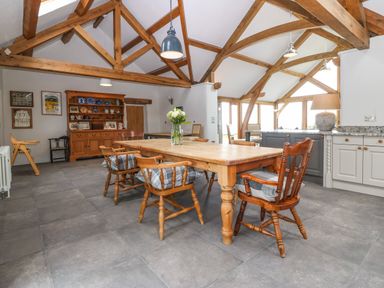 A dining area with a wooden table and chairs under exposed wooden beams at Balog Farm in Amlwch