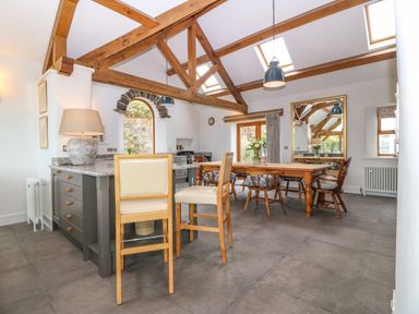 A kitchen and dining area with wooden beams a wooden dining table with chairs and a kitchen island with stools at Balog Farm in Amlwch