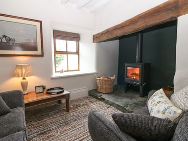 A living room with a wood burning stove a wooden coffee table a window and a framed picture at Balog Farm in Amlwch