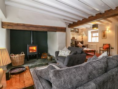 A living room with a wood-burning stove armchairs and a wooden table at Balog Farm in Amlwch