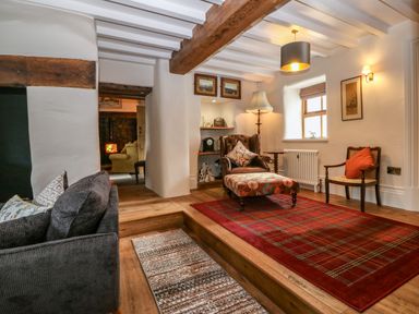 A living room with a sofa cushions armchair ottoman rugs and exposed wooden beams at Balog Farm Amlwch
