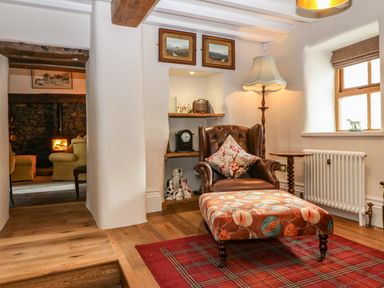 A sitting area with a leather armchair a floral ottoman a floor lamp and shelves with ornaments at Balog Farm in Amlwch