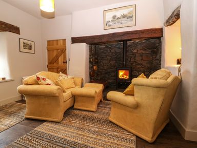 A sitting room with two armchairs an ottoman a rug and a wood burning stove at Balog Farm in Amlwch