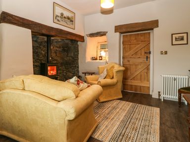 A sitting room with two yellow armchairs a wood burning stove and a wooden door at Balog Farm in Amlwch