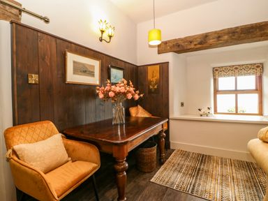 A small dining area with a wooden table flower vase two chairs and a window with a decorative blind at Balog Farm in Amlwch