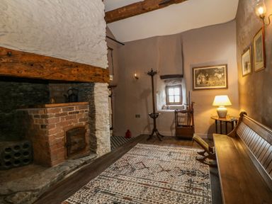 A room with a brick fireplace wooden bench patterned rug and small window at Balog Farm in Amlwch