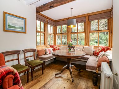 A dining nook with a round wooden table surrounded by a built-in bench and wooden chairs at Balog Farm in Amlwch