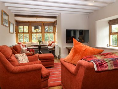A living room with orange sofas a television and a wooden dining nook at Balog Farm in Amlwch