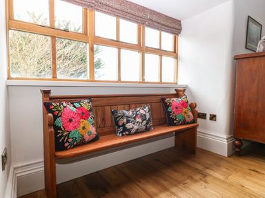 A wooden bench with three floral cushions under a window in a room at Balog Farm in Amlwch