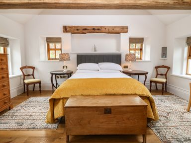 A bedroom with a bed yellow bedspread wooden chest two chairs and two lamps at Balog Farm in Amlwch