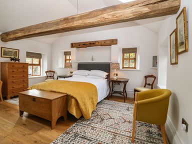 A bedroom with a bed with yellow blanket two windows and wooden furniture at Balog Farm in Amlwch