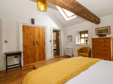 A bedroom with a wooden chest of drawers a yellow chair skylight and a double wooden door at Balog Farm in Amlwch