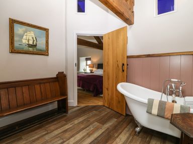 A bathroom with a clawfoot bathtub a wooden bench and a painting of a sailing ship at Balog Farm in Amlwch