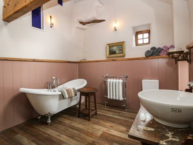A bathroom with a freestanding bathtub a wooden stool a radiator a toilet and a sink with rolled towels on a shelf at Balog Farm in Amlwch