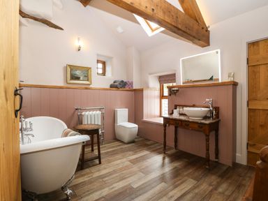 A bathroom with a clawfoot bathtub a wooden sink vanity toilet a small table and exposed wooden beams at Balog Farm in Amlwch
