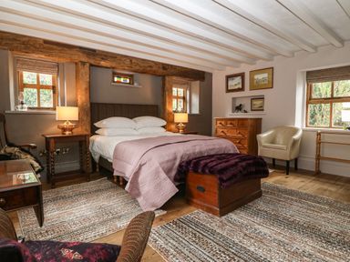 A bedroom with a bed a wooden chest two rugs a dresser and two windows at Balog Farm in Amlwch