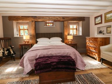 A bedroom with a bed a wooden chest at the foot of the bed wooden furniture and two small windows at Balog Farm in Amlwch